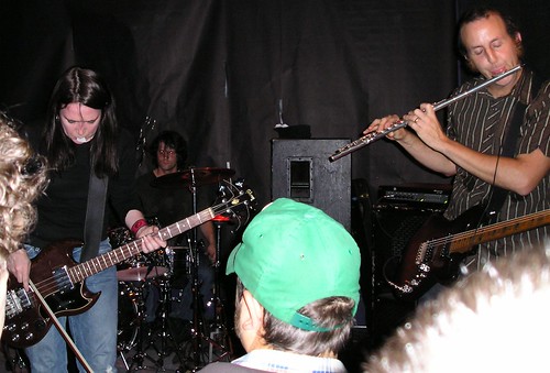 The bassist of Kinski playing an electric bass with a bow and a guitarist of Kinski playing a flute